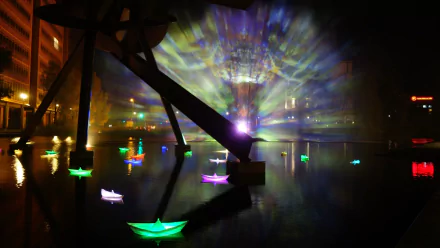 Artistic HD desktop wallpaper capturing vibrant illuminated boats and light beams reflected on water at Berlin's Festival of Lights.