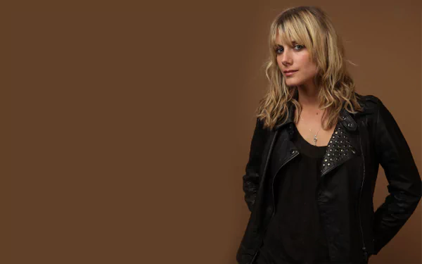 HD desktop wallpaper featuring French actress Mélanie Laurent against a solid brown background, showcasing her casual black outfit and blonde hair.