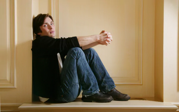 Portrait of Irish actor and celebrity Cillian Murphy sitting against a beige paneled wall, captured in high detail for a 4K Ultra HD PC desktop wallpaper.