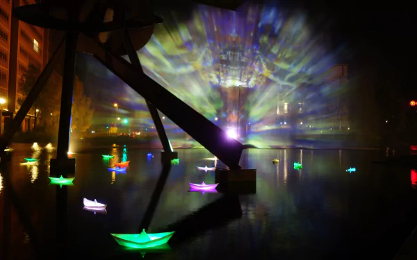 Artistic HD desktop wallpaper capturing vibrant illuminated boats and light beams reflected on water at Berlin's Festival of Lights.