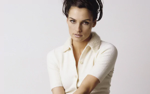 HD wallpaper of Famke Janssen, the Dutch actress, posing against a plain light background with a calm expression, wearing a white top.