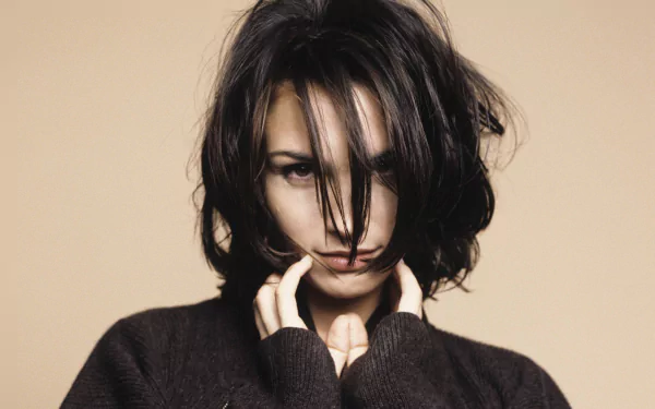 HD desktop wallpaper featuring Dutch actress Famke Janssen with tousled dark hair and a contemplative expression against a neutral background.