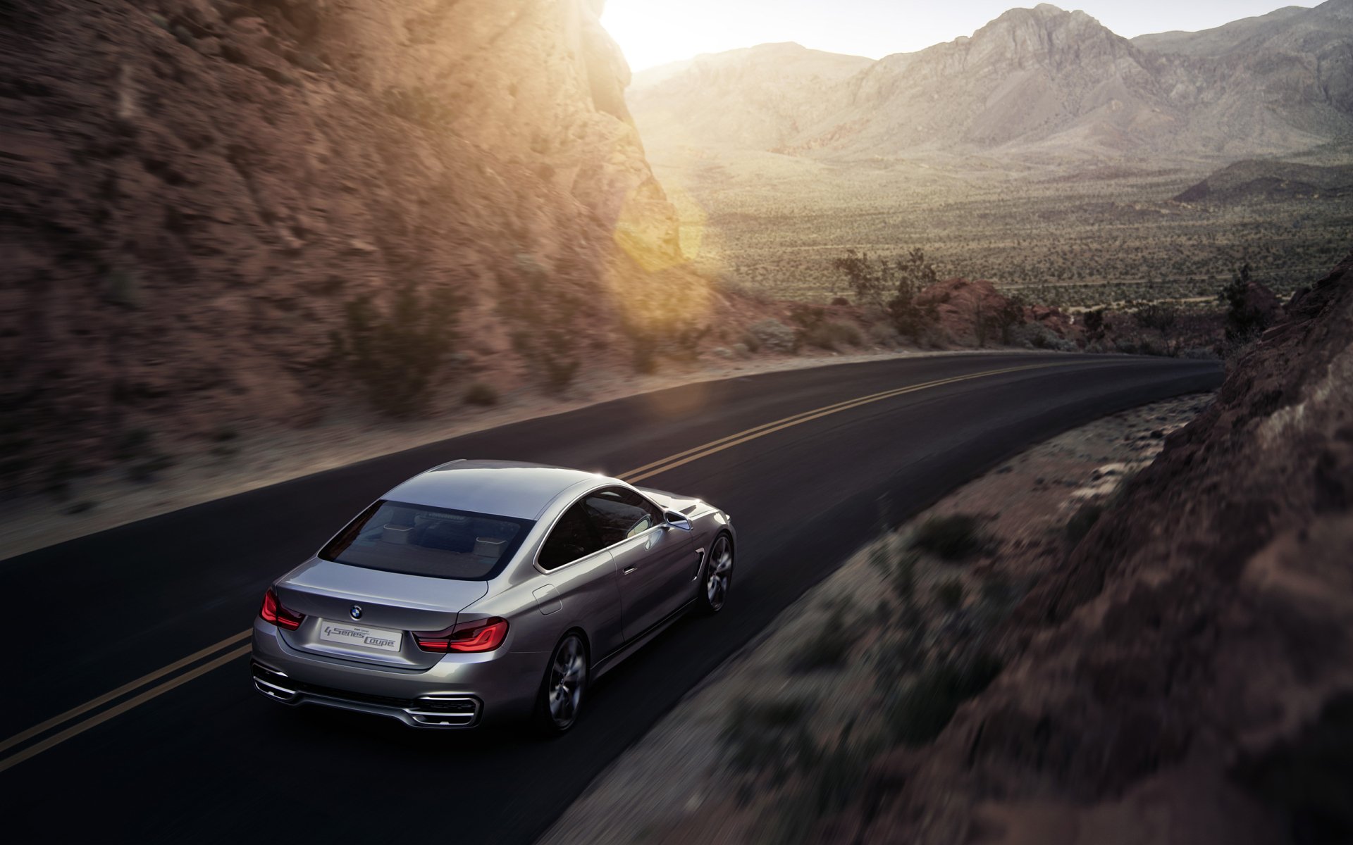 Silver BMW Concept 4 Series Coupé vehicle driving along a winding desert mountain road at sunset — 2K Quad HD PC desktop wallpaper background