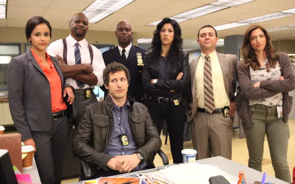 HD desktop wallpaper featuring the cast of Brooklyn Nine-Nine in the precinct, with Jake Peralta (Andy Samberg) seated at the front.