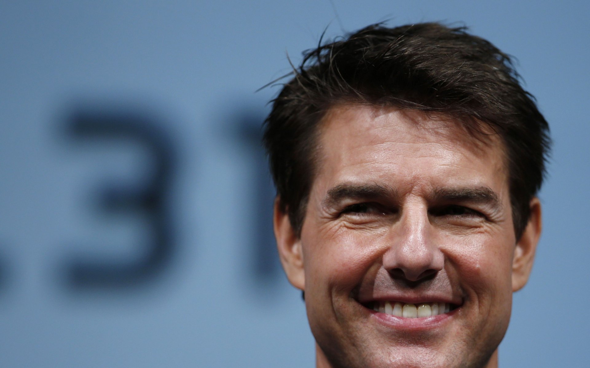 Close-up HD desktop wallpaper of American actor and celebrity Tom Cruise smiling against a blurred background.