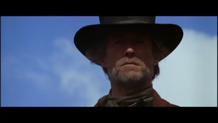 HD PC desktop wallpaper: close-up of a stoic, bearded gunslinger in a wide-brim hat against a bright blue sky — still from the movie Pale Rider.