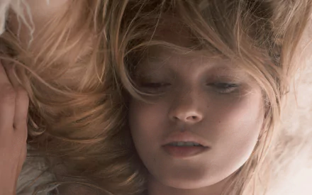 Close-up portrait of a reclining blonde celebrity model with tousled hair and soft lighting — 2K Quad HD PC desktop wallpaper.