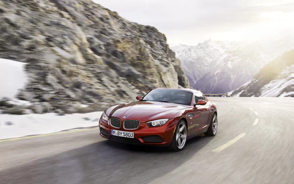 HD desktop wallpaper featuring a red BMW Zagato Coupe driving on a mountain road with rocky cliffs and snow-covered peaks in the background.