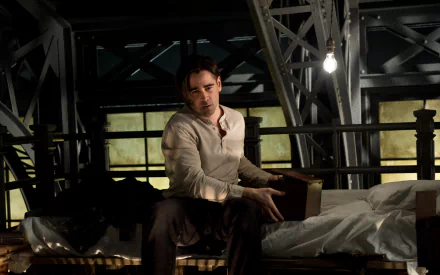 Winter's Tale film still of Peter Lake: brooding man on a metal-framed bed in a dim industrial loft, 2K Quad HD movie desktop wallpaper.