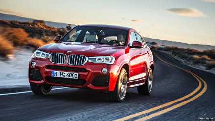 HD PC desktop wallpaper featuring a red BMW X4 driving on a winding road through a desert landscape at sunset.