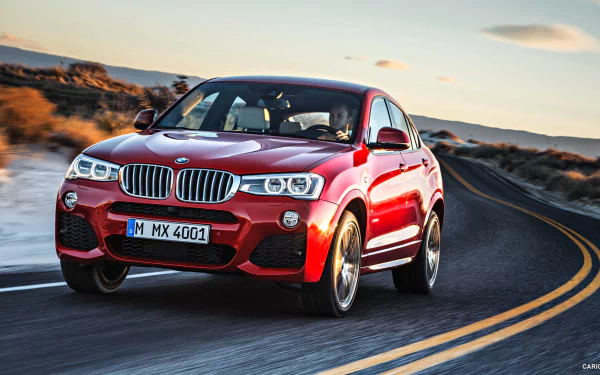 HD PC desktop wallpaper featuring a red BMW X4 driving on a winding road through a desert landscape at sunset.