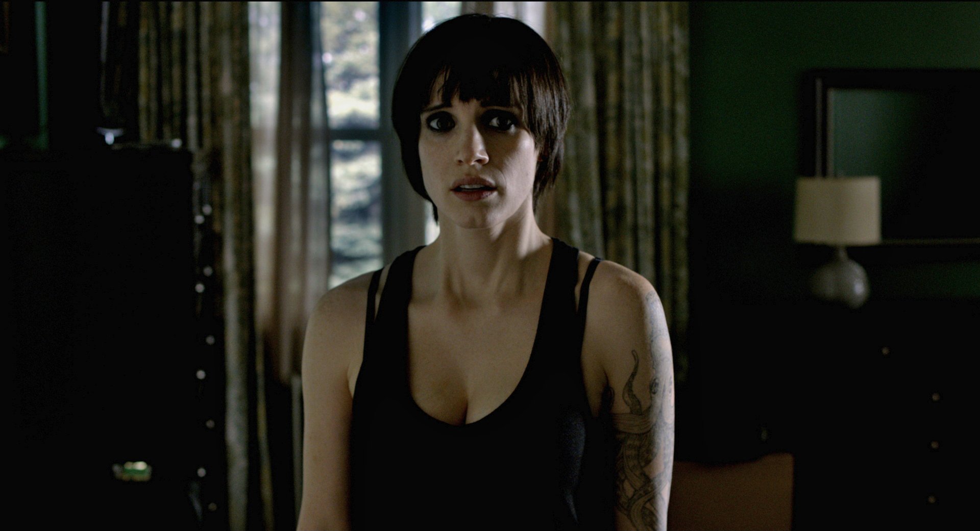 A high-definition desktop wallpaper featuring a tense scene from the movie Mama, showcasing a woman with short hair in a dimly lit room, conveying an atmosphere of suspense.