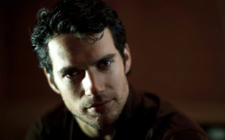 An HD desktop wallpaper featuring British actor Henry Cavill, showcasing a close-up portrait with dramatic lighting and a captivating expression.