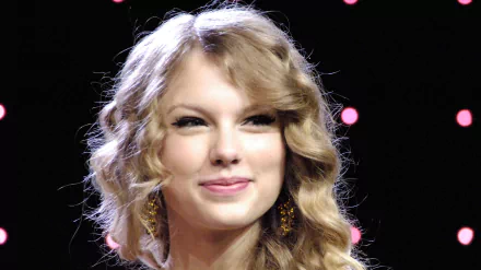 HD desktop wallpaper featuring a close-up of Taylor Swift with wavy blonde hair and earrings, set against a dark background with soft pink lights, highlighting music themes.