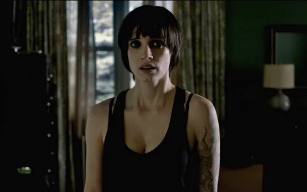 A high-definition desktop wallpaper featuring a tense scene from the movie Mama, showcasing a woman with short hair in a dimly lit room, conveying an atmosphere of suspense.