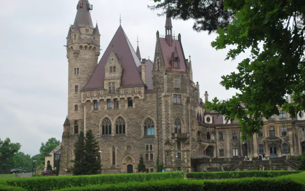 HD PC desktop wallpaper of Moszna Castle — a man-made stone chateau with turrets, steep red roofs and manicured hedges framed by trees.