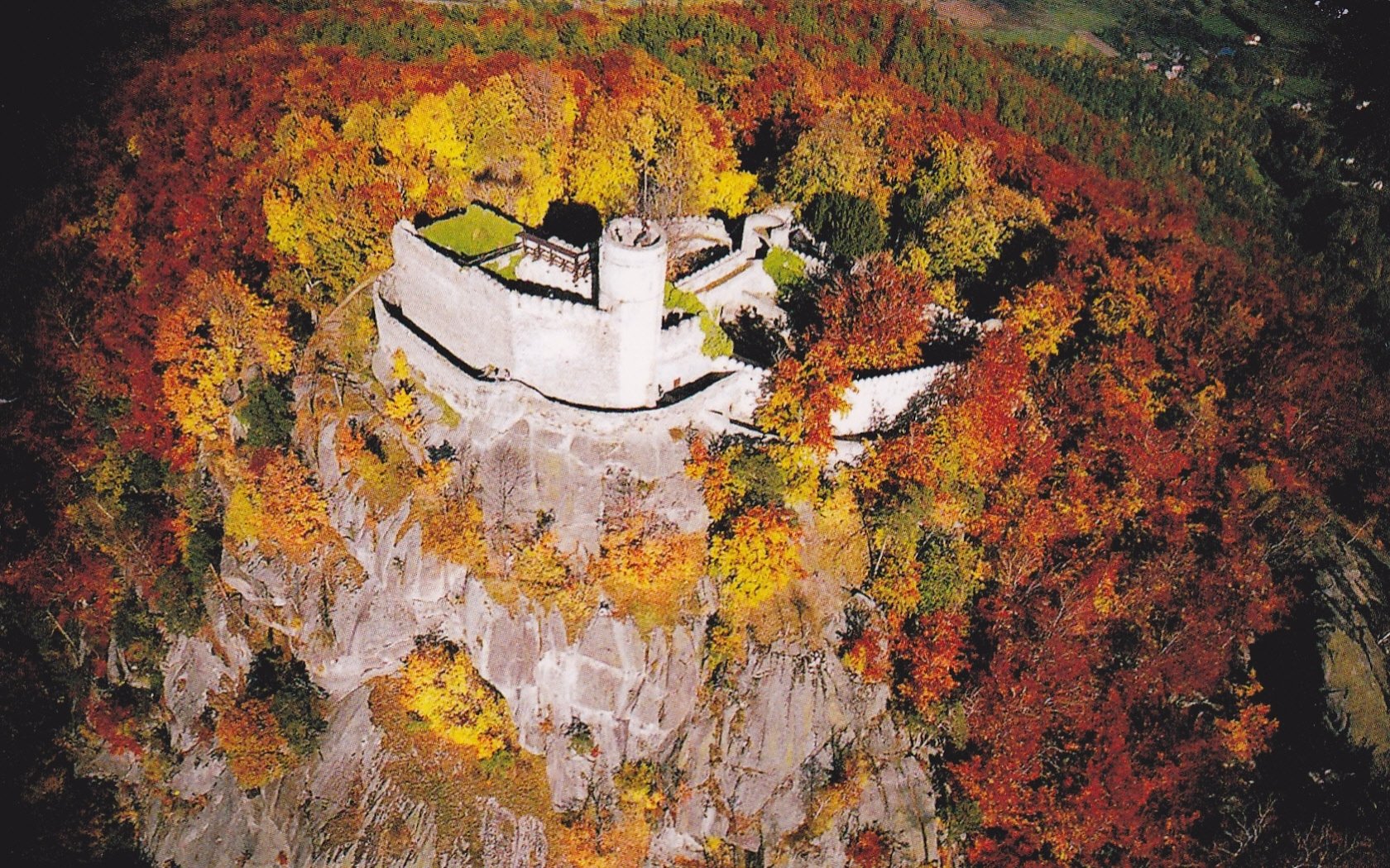 Aerial view of Chojnik Castle, a man-made medieval fortress atop a rocky hill surrounded by colorful autumn trees — HD PC desktop wallpaper background.
