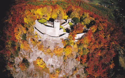 Aerial view of Chojnik Castle, a man-made medieval fortress atop a rocky hill surrounded by colorful autumn trees — HD PC desktop wallpaper background.