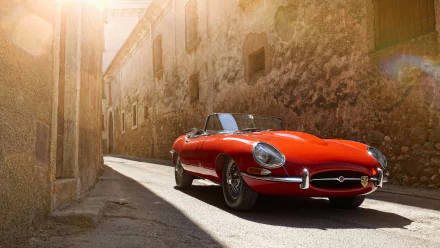 A vibrant red Jaguar E-Type convertible parked on a sunlit cobblestone street, featured as a HD PC desktop wallpaper and background.