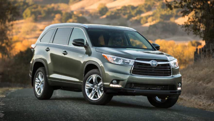 HD PC desktop wallpaper of a Toyota Highlander Hybrid vehicle on a scenic roadside at sunset, three-quarter front view with rolling hills and warm light in the background.