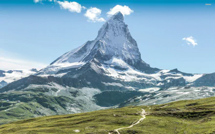 A stunning HD wallpaper of the Matterhorn, showcasing its majestic peak against a clear blue sky, surrounded by lush green valleys and rugged mountain terrain.
