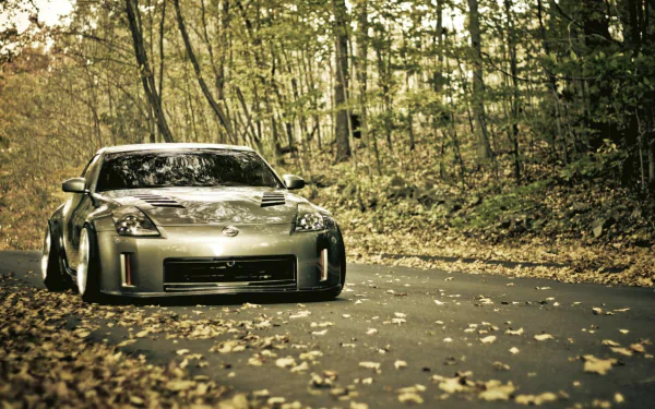 HD PC desktop wallpaper featuring a sleek silver Nissan 350Z parked on a forest road surrounded by autumn foliage.