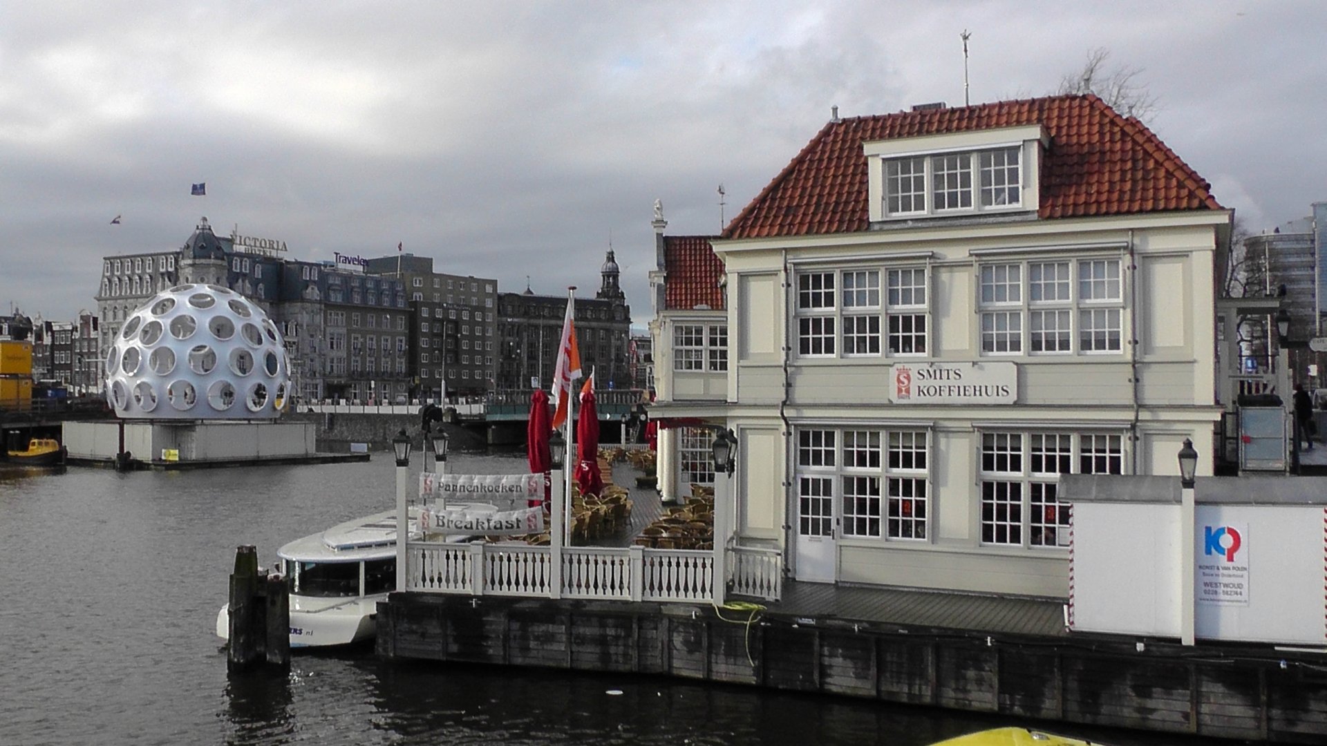 HD desktop wallpaper of a man-made waterfront scene in Amsterdam featuring traditional buildings and a unique floating spherical structure on the canal.