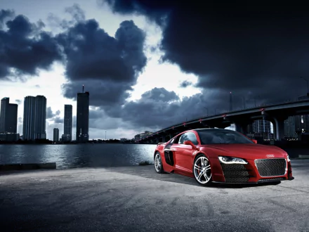 A striking red Audi R8 parked near a waterfront, with a dramatic skyline and stormy clouds in the background. This HD image serves as an impressive desktop wallpaper.