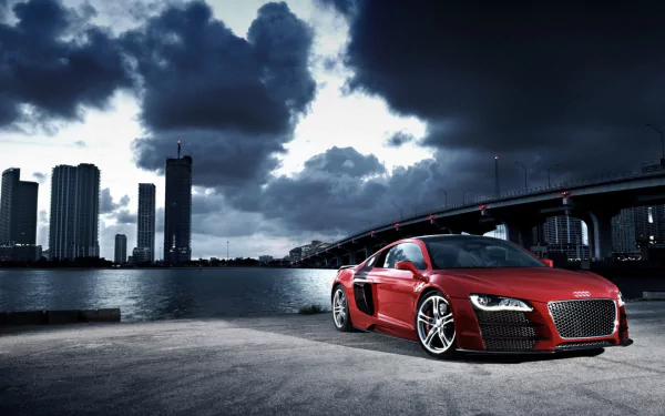 A striking red Audi R8 parked near a waterfront, with a dramatic skyline and stormy clouds in the background. This HD image serves as an impressive desktop wallpaper.