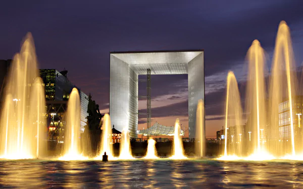 Evening cityscape of La Défense, Paris, showing the illuminated Grande Arche framed by lit fountains — 2K Quad HD PC desktop wallpaper of a man-made urban landmark in France.