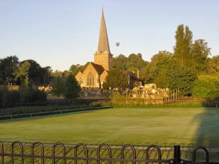 HD desktop wallpaper featuring a serene view of Godalming's historic church surrounded by greenery and a hot air balloon in the sky.