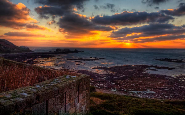 Sunset over rocky coast with man-made Fort Tourgis stone ramparts in foreground, dramatic clouds and tidal pools — 2K Quad HD PC desktop wallpaper/background.