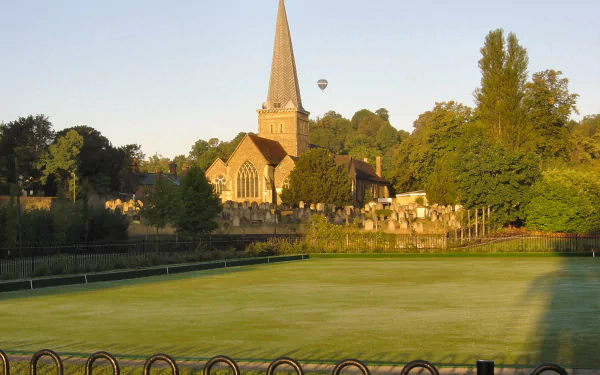 HD desktop wallpaper featuring a serene view of Godalming's historic church surrounded by greenery and a hot air balloon in the sky.