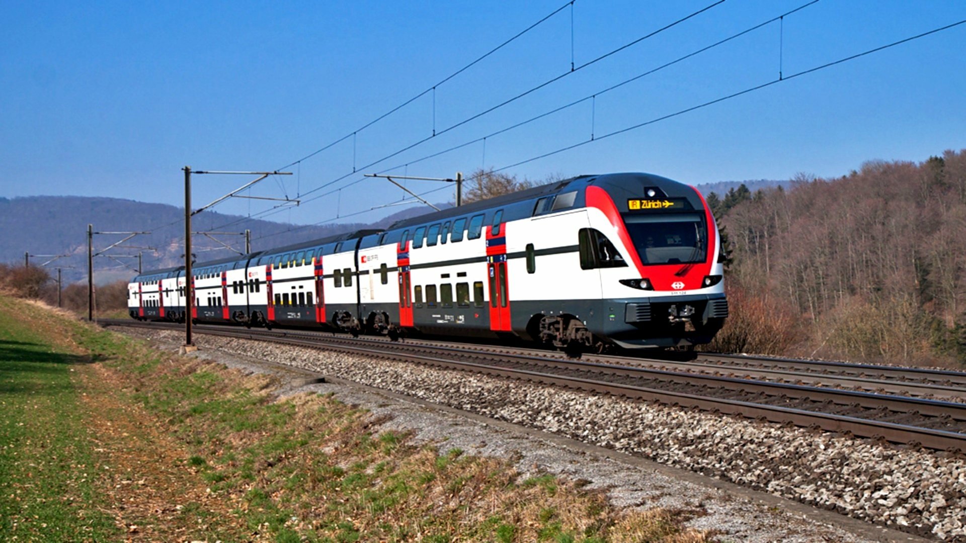 HD PC desktop wallpaper of a modern passenger vehicle — a double-decker train running on electrified tracks through a rural landscape beneath a clear blue sky.