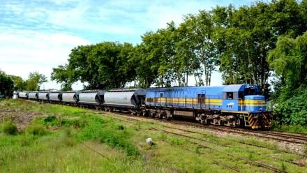HD desktop wallpaper featuring a blue and yellow freight train moving along tracks with green trees and grass under a bright sky.