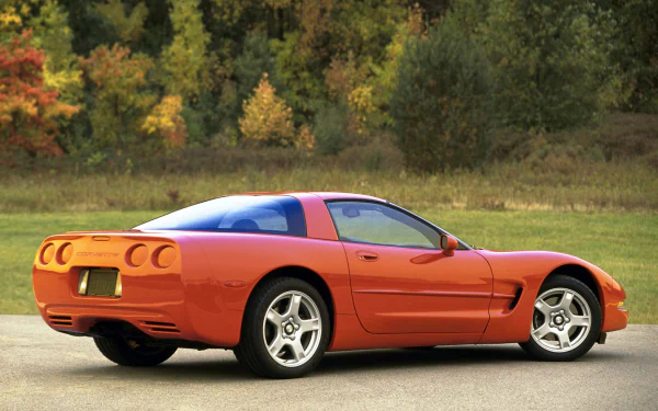 HD PC desktop wallpaper showing a red Chevrolet Corvette (C5) sports vehicle parked on a country road with autumn trees in the background.