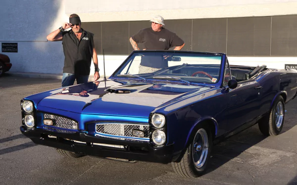 Two men stand beside a classic blue convertible car, featuring sleek lines and chrome details, from the TV show Counting Cars. This image serves as an HD desktop wallpaper and background.