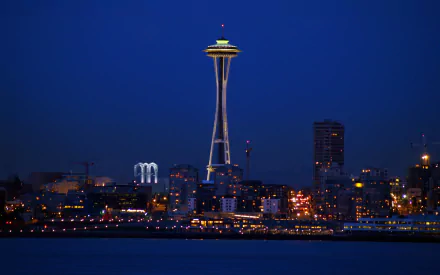 HD PC desktop wallpaper: Seattle skyline at night with the man-made Space Needle illuminated above waterfront city lights against a deep blue sky.