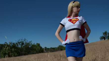 A woman in a vibrant Supergirl cosplay poses confidently in an open field, showcasing her costume against a clear blue sky. This HD image serves as a striking desktop wallpaper.
