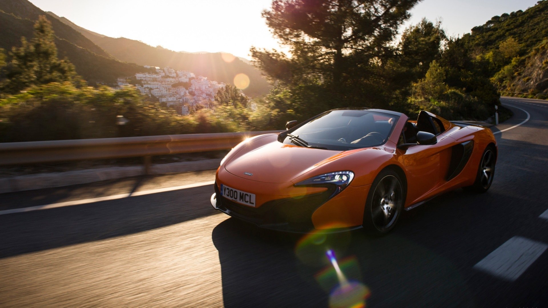 Orange McLaren 650S Spider supercar driving along a sunlit coastal road at sunset — HD PC desktop wallpaper and background.