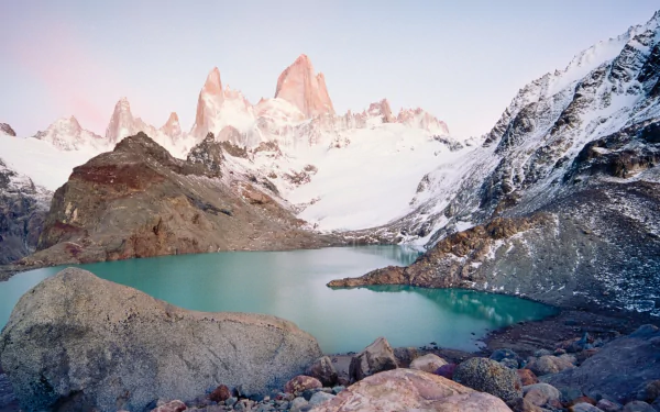 Nature HD PC desktop wallpaper and background: Mount Fitz Roy rising above a turquoise glacial lake, rocky foreground and snow-capped peaks beneath a pastel sunrise sky.