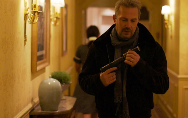 HD PC desktop wallpaper from the movie 3 Days to Kill: a man in a coat and scarf inspects a handgun while walking down a hotel hallway.