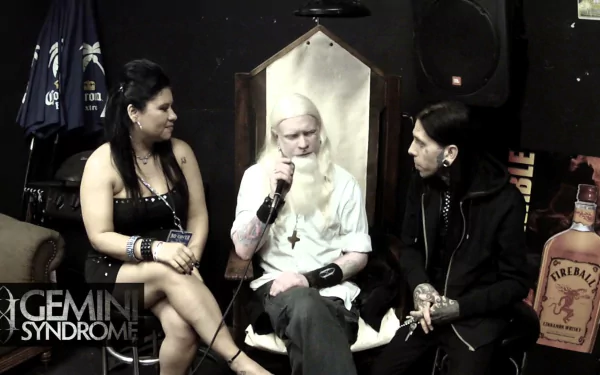 HD desktop wallpaper featuring three people in a casual interview setting, with the Gemini Syndrome logo displayed.