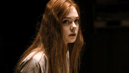 HD PC desktop wallpaper: cinematic close-up of a red‑haired young woman in dim, moody lighting with a pensive expression and film‑style background.
