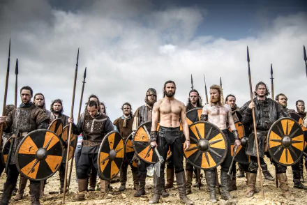 HD desktop wallpaper from Vikings (2013) TV show featuring Rollo and warriors holding round shields in a battle-ready stance under a cloudy sky.