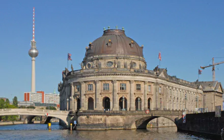 HD desktop wallpaper showcasing the Bode Museum, a grand man-made historic building by the river, with Berlin's TV tower visible in the clear blue sky.