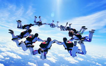 A dynamic skydiving scene features a group of jumpers forming a circle against a bright blue sky, showcasing the thrill of the sport in this HD desktop wallpaper.