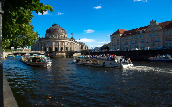 HD desktop wallpaper showing man-made Bode Museum along a sunny river with boats cruising under blue skies.