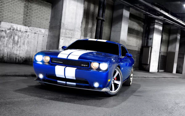 HD PC desktop wallpaper: blue Dodge Challenger SRT8 muscle vehicle with white racing stripes, headlights on, parked in a dim industrial garage.