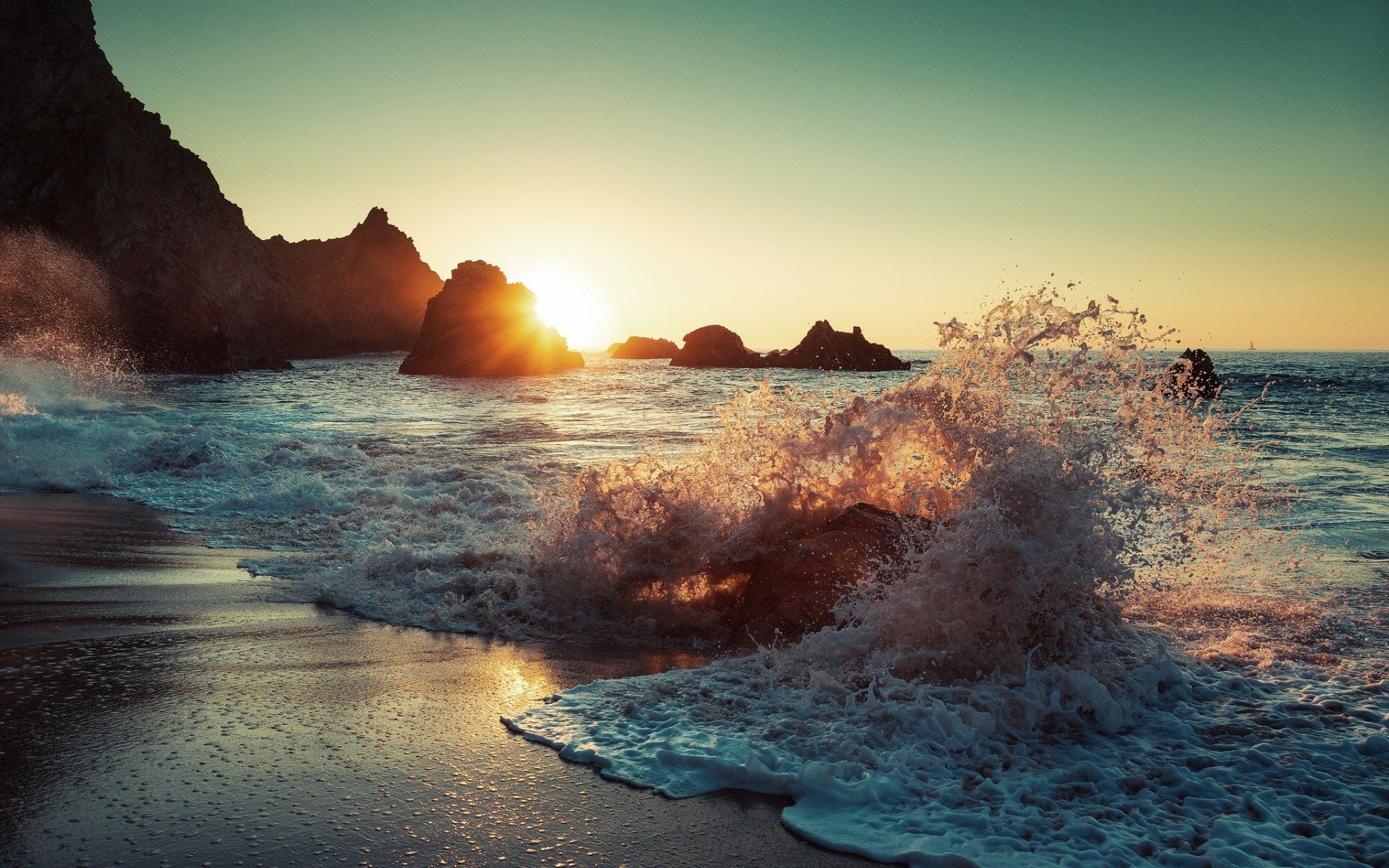 HD PC desktop wallpaper of a serene beach at sunset with waves crashing against rocky cliffs under a clear sky.